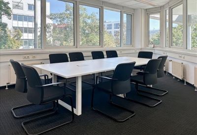 Professional conference room with a long white table, black chairs, and large windows with garden views.