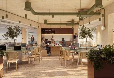 Spacious coworking area with wooden furniture, indoor trees, and industrial exposed ceiling ducts.
