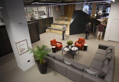 Open communal lounge featuring orange armchairs, a large grey sectional sofa, and a tiered wooden seating area.