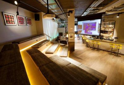 Breakout space with tiered wooden bleacher seating facing a large presentation screen and bar counter.