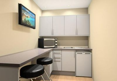 Compact communal kitchenette with a breakfast bar, stools, microwave, and small refrigerator.