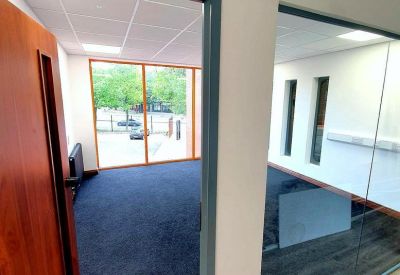 Modern empty office space with grey carpeting and large windows providing natural light.