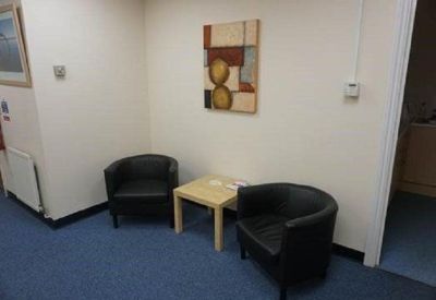 Reception area with black tub chairs, a wooden side table, and modern wall art.
