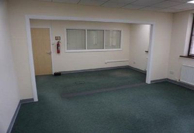 Spacious green-carpeted office room with an open doorway and wall-mounted fire extinguisher.