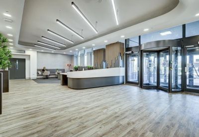 Spacious lobby with light wood flooring, revolving door entrance, and linear ceiling lighting.