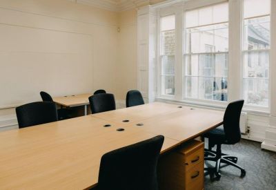 Bright office space with two large windows and a six-person cluster of wooden desks.