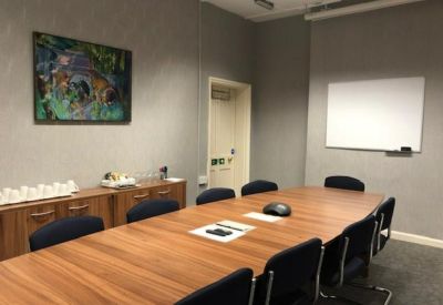 Professional boardroom with a large wooden table, blue chairs, and a whiteboard.