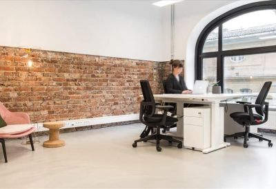 Bright office with adjustable desks, ergonomic chairs, and a feature brick wall.