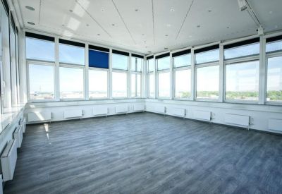 Sun-drenched, empty corner office space with wrap-around windows and wood-laminate flooring.