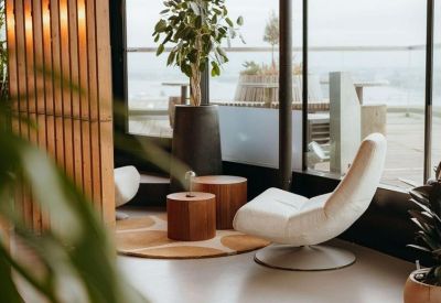 Modern lounge area with white swivel chairs, wooden side tables, and large windows.