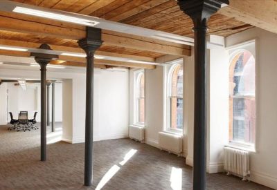 Spacious open-plan office with exposed wooden ceilings and industrial iron columns.