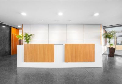Modern reception area with light wood panelled desk and indoor plants.