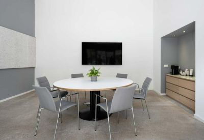 Bright conference room with a round white table and integrated media screen.