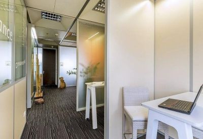 Small private office suite featuring a white desk, laptop, and glass partitions.