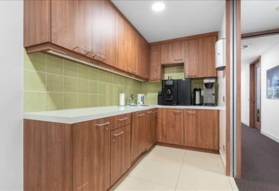 L-shaped kitchen area with wood cabinets, green tiled backsplash, and coffee machines.