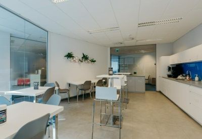 Bright office kitchen with white cabinetry and multiple dining tables.