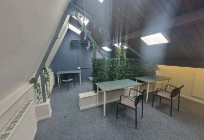 Bright attic workspace with communal tables and green privacy hedging.
