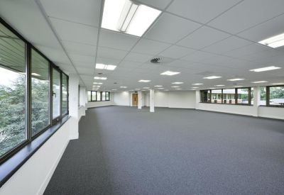 Spacious, empty open-plan office floor with grey carpeting and large windows.