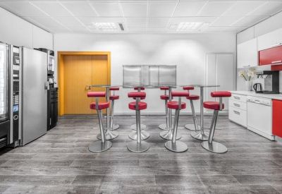 Modern breakout kitchen area with red bar stools and sleek white cabinetry.