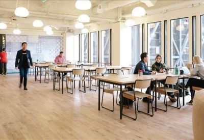 Open-plan dining and work area with rows of wooden tables under spherical light fixtures.