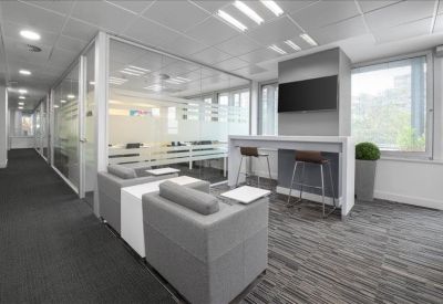 Lounge area with grey armchairs, a high breakfast bar, and glass-partitioned offices.