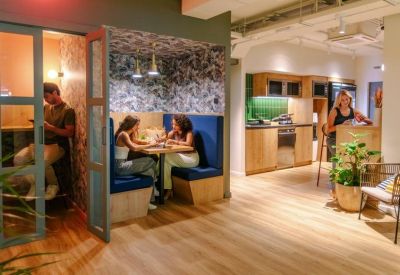 Vibrant communal area with private wooden booths, a modern kitchen, and warm lighting.