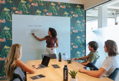 Bright meeting room featuring a tropical leaf-patterned feature wall and people brainstorming at a table.