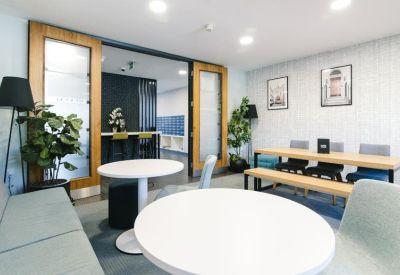 Open communal kitchen and breakout area with round tables, light grey sofas, and wooden door accents.