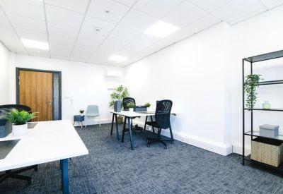Bright private office featuring two white desks, black ergonomic chairs, and a tall minimalist shelf unit.