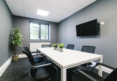 Modern meeting room with a white conference table, grey textured feature wall, and a wall-mounted television.