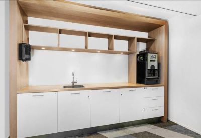 Sleek kitchenette with wooden cabinetry, coffee machine, and white counters.