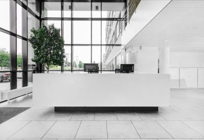 Minimalist white reception desk in a lobby with floor-to-ceiling glass windows.