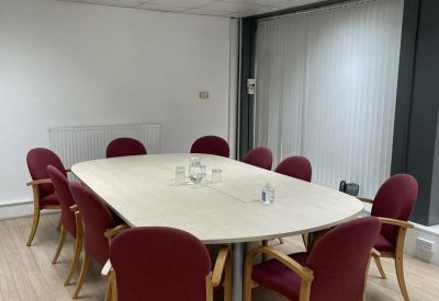 Meeting room with a large oval table, burgundy chairs, and wooden flooring.