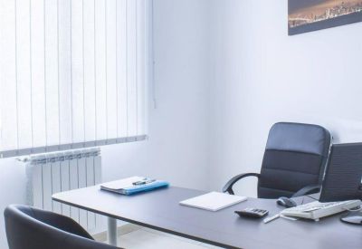 Private office at Piazza Carità, featuring two dark armchairs and a desk with a laptop near a large window.