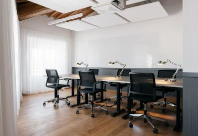 Bright office space with a long shared desk, ergonomic chairs, and individual task lamps.
