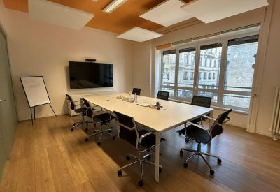 Modern meeting room featuring a white table, black chairs, and a large wall-mounted monitor.