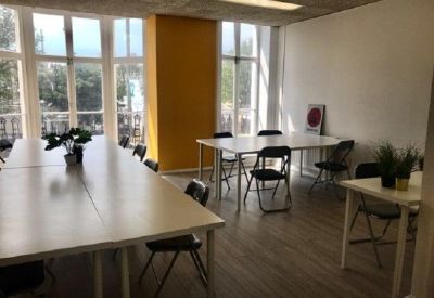 Large open-plan workspace with long white tables and bright yellow accent wall.