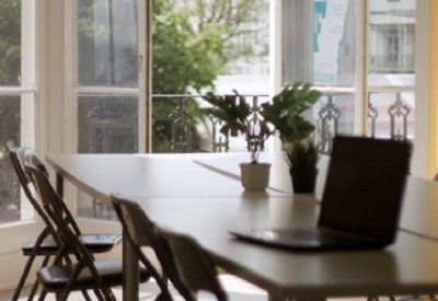 Meeting area with white tables, folding chairs, and potted plants in front of a balcony.
