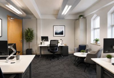 Bright private office featuring a grey lounge area and modern white workstations.