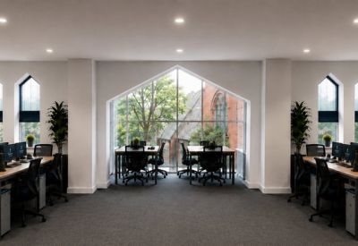 Open-plan workspace with multiple desks and a large glass-fronted gable window.