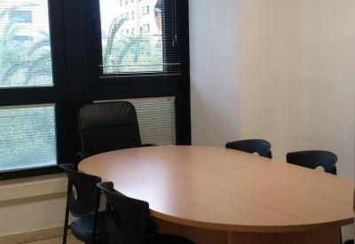 Meeting room with a wooden oval table, black chairs, and large windows overlooking the city.