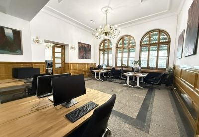 Spacious open-plan office with wooden desks and large arched windows.