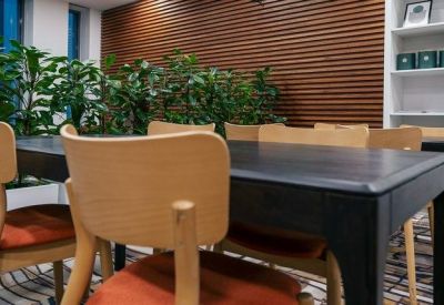 Shared workspace with dark tables, orange upholstered chairs, and a slatted wood feature wall.