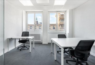 Bright two-person office with white desks and city views through large windows.