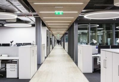 Bright hallway lined with white desks, ergonomic chairs, and circular ceiling lights.