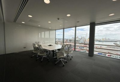 Modern meeting room with a white table and mesh chairs overlooking industrial harbor views.