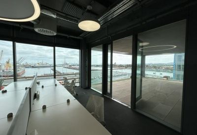Open-plan office desks with views of a harbor and access to an outdoor terrace area.