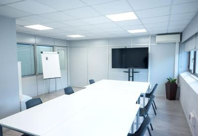 Spacious meeting room with a large white table, wall-mounted screen, and flipchart.