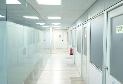 Bright white corridor with glass-partitioned offices and a fire extinguisher.