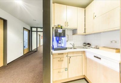 Office kitchenette area with light wood cabinets and a professional coffee machine.